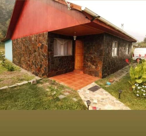 a stone house with a red roof and a yard at lindo lugar, cabaña paso nevado in Colbún Alto