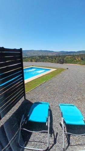 two blue chairs sitting next to a bench with a pool at Grado8punto8 Glamping Valle de Los Artistas in Lolol