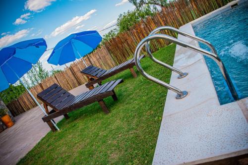 two benches with umbrellas next to a swimming pool at Cabañas 2Tierras in Chicoana