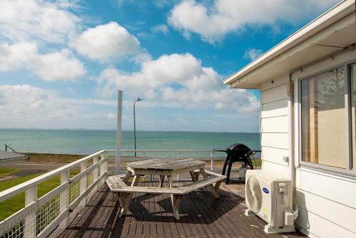 a picnic table on a deck with a view of the ocean at Stunning beachfront bach! in Manukau Heads