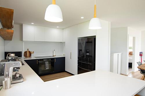 a kitchen with white cabinets and black appliances at Stunning beachfront bach! in Manukau Heads