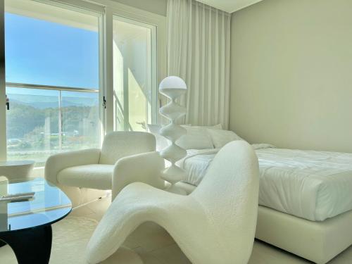 a white bedroom with a bed and a chair and a table at Le Bleu Naksan by Orot in Yangyang