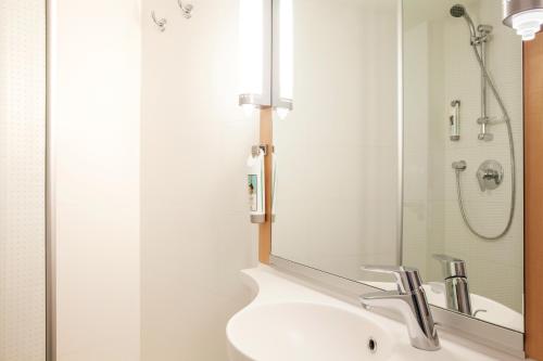 ein Bad mit einem Waschbecken und einer Dusche mit einem Spiegel in der Unterkunft ibis Basel Bahnhof in Basel
