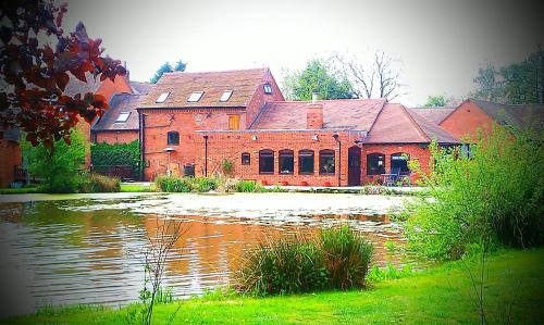 a large red brick building next to a body of water at Malswick Mill in Newent