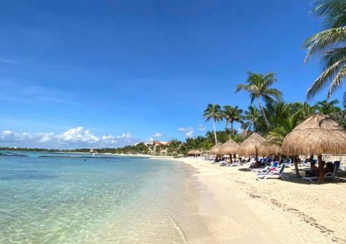a beach with straw umbrellas and chairs and the ocean at High-End Waterfront Condo at Secrets Waters in Puerto Aventuras