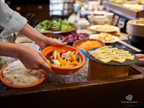 eine Person, die eine Schüssel Essen auf einer Theke hält in der Unterkunft Daiwa Roynet Hotel Sapporo-Susukino in Sapporo