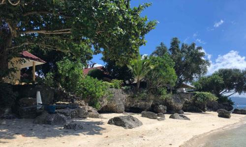 a beach with rocks and trees and a house at Tipolo Guesthouse in Basdiot
