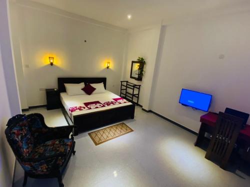 a bedroom with a bed and a chair and a television at Ceylon Avenue in Habaraduwa