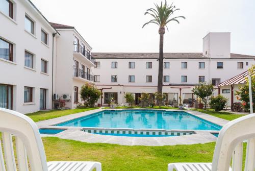 a pool in the courtyard of a building with two chairs and a palm tree at Hotel Francisco De Aguirre in La Serena