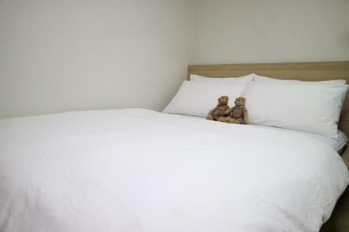 two teddy bears sitting on top of a white bed at Mr. Kim Guesthouse in Incheon