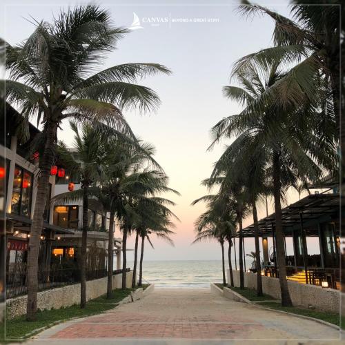 a row of palm trees on a sidewalk near the ocean at Canvas Danang Beach Hotel in Da Nang