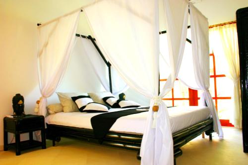 Un dormitorio con una cama con dosel y cortinas blancas. en Villa Anaïs Jardin Paradisiaque Face à la Mer, en Banjar