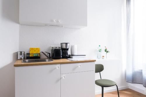 a white kitchen with a counter and a chair at Hostel MaRu Living C9 in Cologne