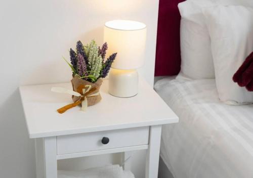 a white nightstand with a lamp and flowers on a bed at Comfortable 3 Bedrooms Leeds Beach House - Ideal for Family and Contractors - Free WIFI, Projector in bedroom and Free Parking for 2 cars in Killingbeck