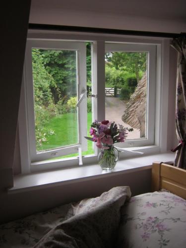 a vase of flowers sitting on a window sill at THE MOATS - CODDINGTON A small private thatched cottage B&B located in quiet countryside between Ledbury and Malvern - convenient for the Malvern Three Counties Showground and 5 miles from excellent shops restaurants and Ledbury Poetry Festival in Ledbury