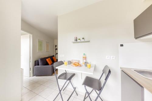 une cuisine et un salon avec une table et des chaises blanches dans l'établissement Le Haven Stade de France renty, à Saint-Denis