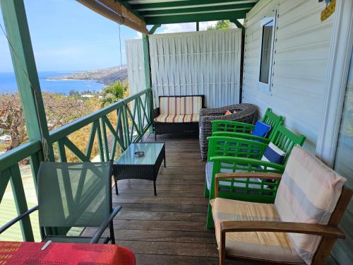 a porch with chairs and tables and a view of the ocean at Chalet Sunset, vue panoramique sur la baie, proche de Saint-Leu et ses plages in Saint-Leu