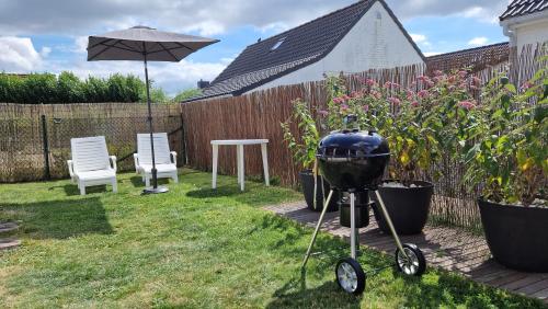 a grill in a yard with two chairs and an umbrella at Vissershuisje 89 te Wenduine in Wenduine