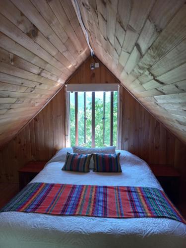 a bed in a wooden room with a large window at Cabaña Conguillio Chercan con refrigerador in Conguillio