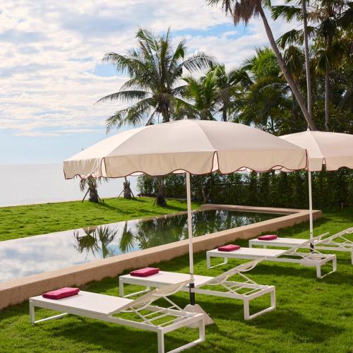 a row of lounge chairs and umbrellas by a pool at Mahi-Mahi Beachfront Villa by Yudee Assets in Cha Am