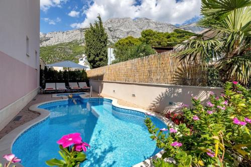 a swimming pool with flowers and mountains in the background at Apartmani Podest in Baška Voda