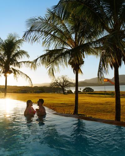 two women sitting in a swimming pool with palm trees at Pousada Terramare in Guapé