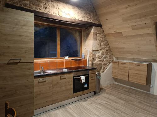 une cuisine avec des armoires en bois, un évier et une fenêtre dans l'établissement La Terrasse Bleue, havre de paix avec vue sur le Célé, à 15 min de Figeac, à Corn