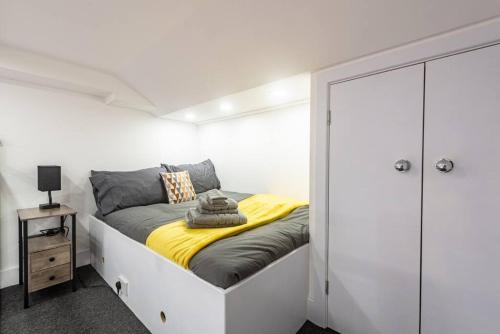 a white bedroom with a bed with a yellow blanket at Studio in Central Reading- Next to Town Centre in Reading