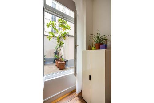 Cette chambre dispose d'une fenêtre et d'une armoire blanche avec des plantes. dans l'établissement Chic & bright studio Saint-Georges, à Paris