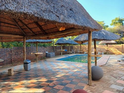 a pavilion with tables and umbrellas next to a pool at Kadichueni Guest House in Zeerust
