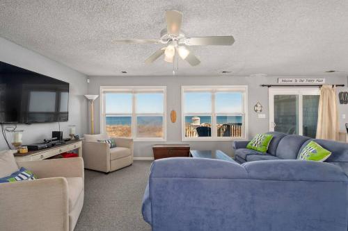 a living room with a blue couch and a ceiling fan at OBX 4BR Oceanfront Cottage in Kill Devil Hills