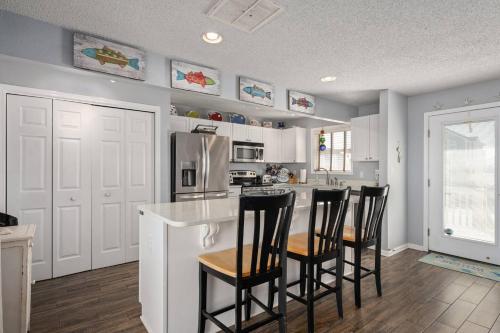 a kitchen with white cabinets and black bar stools at OBX 4BR Oceanfront Cottage in Kill Devil Hills