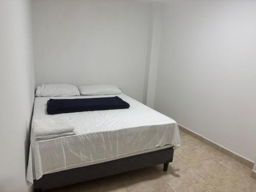 1 dormitorio con 1 cama con sábanas blancas y manta azul en Acogedor Apartaestudio cerca al centro Armenia 3, en Armenia