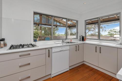 a kitchen with white cabinets and windows at Sea Serenity - Ruakaka Holiday Home in Ruakaka