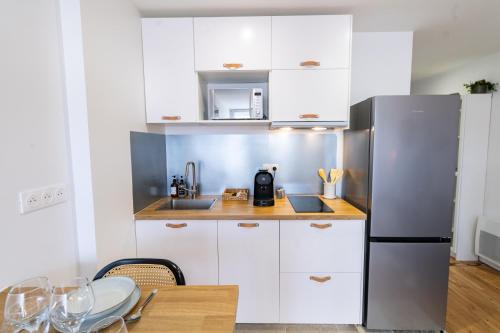 une cuisine avec des armoires blanches et un réfrigérateur en acier inoxydable dans l'établissement Prestige by Opera - Votre évasion cosy à Toulouse - Centre ville - Wifi - Bureau, à Toulouse