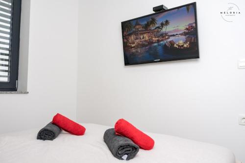 two red pillows on a bed with a tv on the wall at Meloria Apartments in Veržej