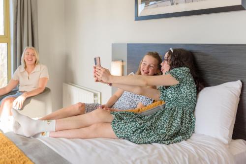 two women are sitting on a bed taking a picture at Newtown Park Hotel in Wexford
