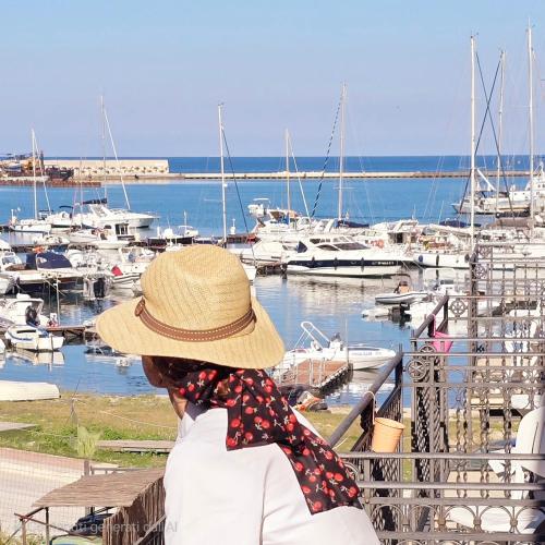 a woman sitting on a bench looking at a marina at Hotel Cala Marina in Castellammare del Golfo
