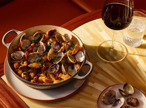 a pan of mussels on a table next to a glass of wine at The Manner, The Unbound Collection by Hyatt in New York