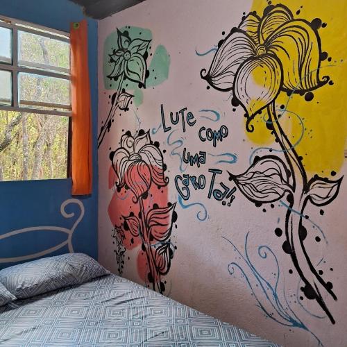 a bedroom with a wall with flowers painted on it at Quarto em Casa João e Maria STL in São Thomé das Letras