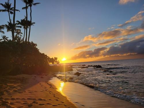 a sunset on a beach with palm trees at Napili Shores - Ocean Front Ground Floor in Kahana