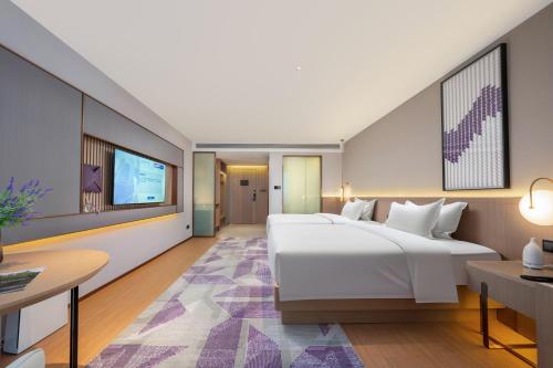 a bedroom with a large white bed and a table at Lavender Hotel Xinle Shijiazhuang Airport Hebei Academy of Fine Arts in Xinle