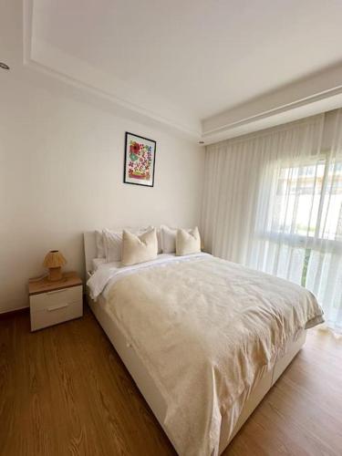 a white bedroom with a large bed and a window at Luxury Garden Apartment by the Beach in Tamraght Ouzdar