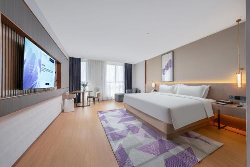 a hotel room with a bed and a flat screen tv at Lavender Hotel Xinle Shijiazhuang Airport Hebei Academy of Fine Arts in Xinle