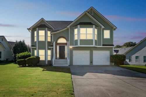 a large green house with a garage at Modern 6BR Haven with Playroom, Gym & Deck! home in Cartersville