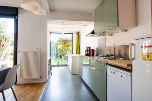 une cuisine avec des appareils blancs et une grande fenêtre dans l'établissement Maison à l'orée du BOIS CITADELLE de LILLE avec TERRASSE en plein sud PROCHE DE TOUTES COMMODITES à la porte de LILLE, à Lambersart