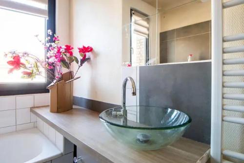 un bagno con lavandino in vetro e fiori su un bancone di Maison à l'orée du BOIS CITADELLE de LILLE avec TERRASSE en plein sud PROCHE DE TOUTES COMMODITES à la porte de LILLE a Lambersart