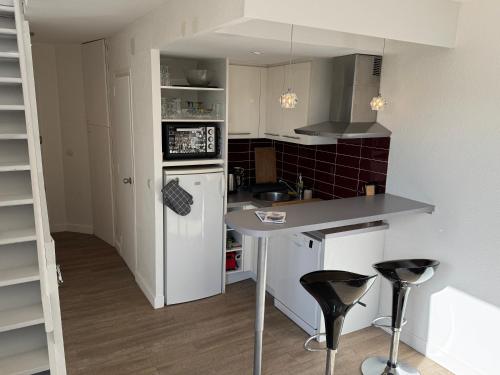 Il comprend une cuisine équipée d'un réfrigérateur blanc et d'un comptoir avec tabourets. dans l'établissement Le Solarium au bord des flots, à Sète