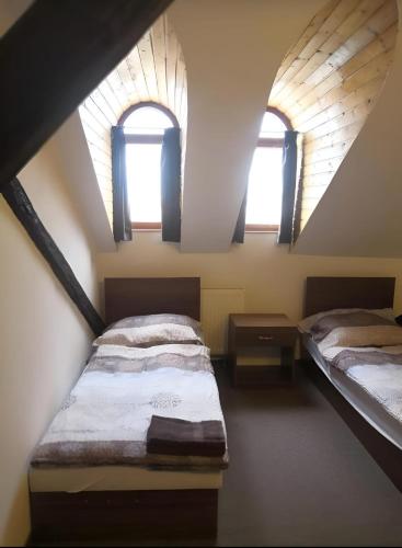 two beds in a attic room with two windows at Hotel Zlatý Anděl in Žatec