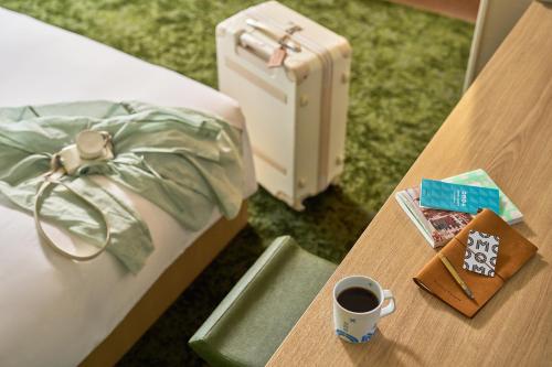 a bed and a table with a cup of coffee and a suitcase at OMO Kansai Airport by Hoshino Resorts in Izumi-Sano